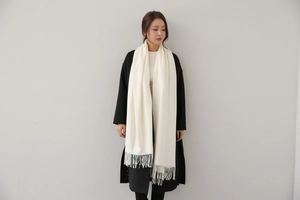 Detailed view of long cream white cashmere-feel scarf with fringe worn by a model