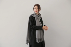 Detail of gray knitted cashmere scarf with tassel fringe worn by a model in black coat