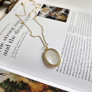 Vintage gold 925 sterling silver necklace featuring an oval white shell pendant on a book