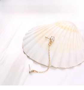 Detail of gold chain earring with sparkling zircon clusters on marble and shell background