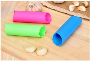 Trois éplucheurs d'ail en silicone rose, vert et bleu sur une planche à découper