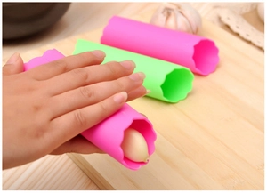 Éplucheurs d'ail en silicone rose et vert sur une planche à découper en bois