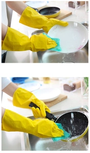 Detail of yellow latex gloves being used to wash dishes with a green sponge in kitchen sink