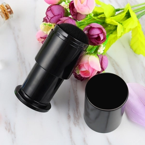 Portable retractable makeup brush with black bristles and matching lid on marble surface