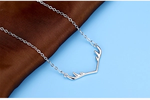 Close-up of silver-plated elk antler pendant necklace on smooth silk fabric