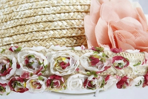 Close-up of woven straw hat featuring a large pink mesh flower and floral ribbon detail