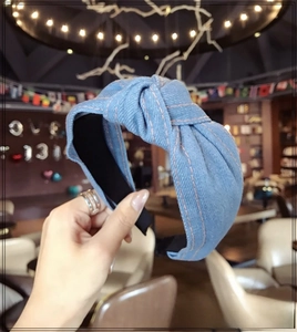 Detail view of light blue denim knot headband with contrast orange stitching design