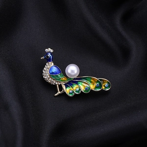 Macro detail of luxury peacock brooch featuring emerald enamel and white pearl inlay