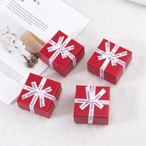 Top view of four red square jewelry gift boxes with white ribbons on soft white plush surface