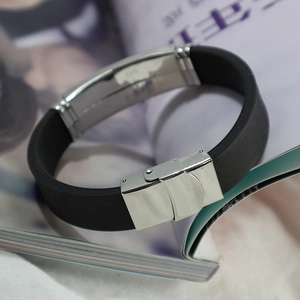 Men's minimalist black silicone bracelet with stainless steel clasp on a magazine background