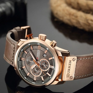Detail view of rose gold chronograph watch with dark gray dial and brown leather strap