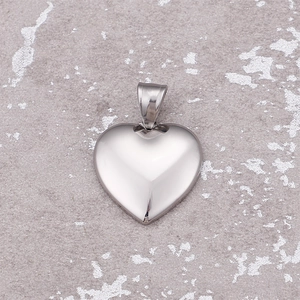 Pendentif en forme de cœur en acier inoxydable poli sur un fond de pierre grise minimaliste