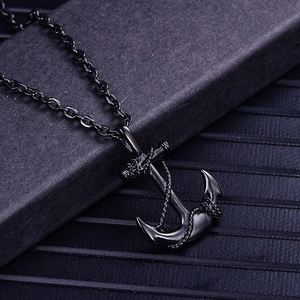 Close-up of black plated titanium steel anchor pendant necklace with metallic chain on black texture