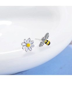 Close-up of asymmetric flower and bee stud earrings with pavé crystals on white porcelain