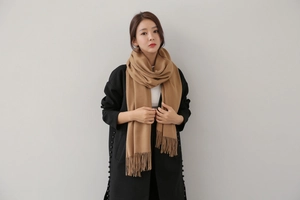 Close-up of a long camel cashmere scarf with fringe details worn over a black coat