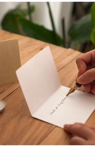 Close-up of handwriting on minimalist cream greeting card with pen on wood table