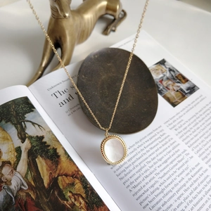 Detail of vintage oval shell pendant on gold cable chain resting on art books