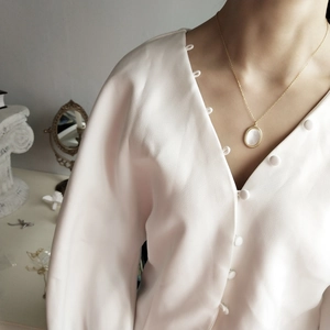 Detail of a gold oval shell pendant necklace worn on a model in a vintage setting