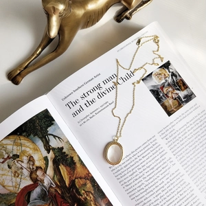 Detailed close-up of a golden oval shell pendant necklace on an open art book