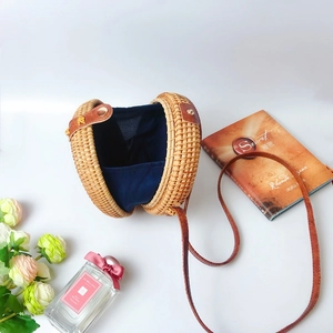 Detail of round woven rattan bag with blue fabric lining, brown leather strap and metal clasp