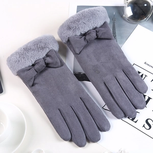 Detail von grauen Damen-Wildlederhandschuhen mit Plüschbündchen und Schleife auf weißem Tisch