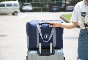 Detail of navy blue foldable travel bag secured on luggage trolley handle outdoors