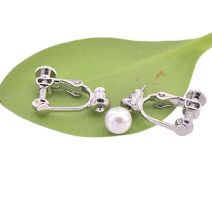 U-shaped silver earring converter with white pearl on green leaves with white background