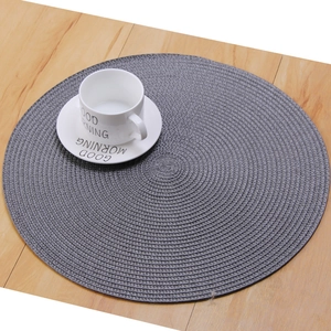 Gray round woven placemat on a wooden table with a white coffee cup for breakfast