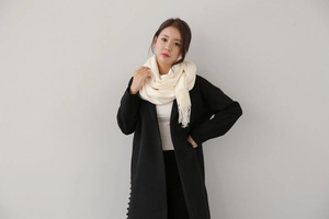 Detail of cream cashmere-style scarf with tassel fringe paired with black wool coat