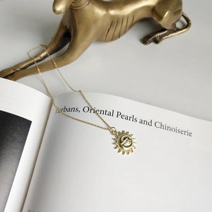 Detail of gold moon and sun pendant necklace laid on an open book with elegant props
