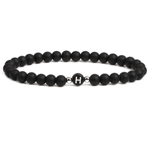 Macro detail of black matte stone bracelet with letter H bead and silver spacers