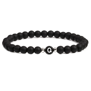 Detail of matte black beaded bracelet featuring white letter Q charm and silver accents