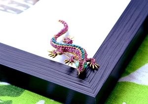 Macro shot of a gold gecko brooch with pink and blue crystals on a frame corner