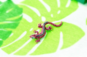 Detailed view of gold lizard brooch with pink and blue crystals on tropical leaf fabric