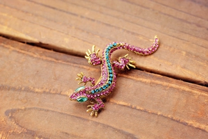 Close-up of colorful gecko brooch with pink, blue and green crystals on wooden surface