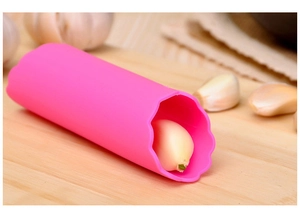 Détail d'éplucheur d'ail en silicone rose sur planche en bois avec gousses d'ail
