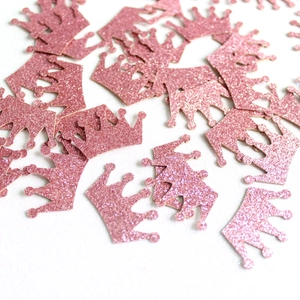 Pink glitter crown confetti scattered on white background for party table decoration
