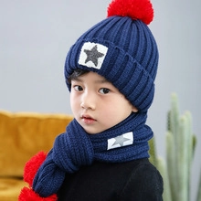 Close-up of deep blue knitted hat and scarf set with red pom-poms and star patches