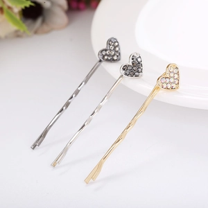 Close-up of three sparkling rhinestone heart bobby pins in gold, silver, and grey finishes