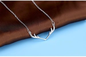 Close-up of elegant silver necklace with antler pendant on luxurious silk fabric
