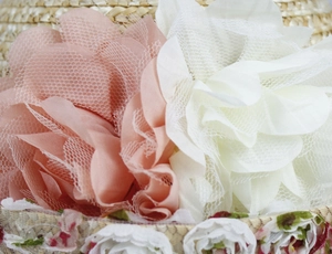 Macro detail of handmade fabric floral decorations and lace on a straw sun hat