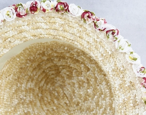 Close-up of hand-woven straw hat detail with delicate red and white fabric rose accents