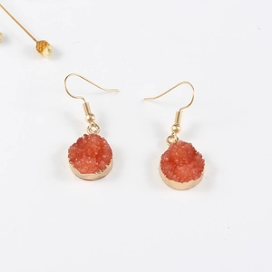 Detalle de pendientes redondos de resina naranja con bordes de metal dorado en fondo blanco