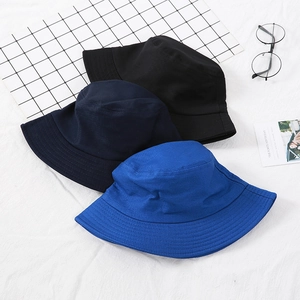 Flat lay of cotton bucket hats in black, navy, and bright blue on white textured fabric