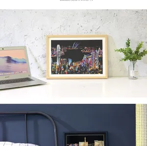 City night scene scratch art kit in a light wood frame on a modern office desk setup