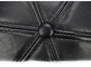 Macro shot of 6-panel stitching and top button detail on a black leather baseball cap