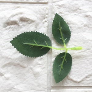 Artificial deep green rose leaves with three-pronged structure on white brick background