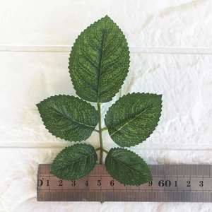 Detail of artificial green rose leaves with lifelike veins and serrated edges next to a ruler