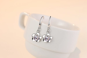 Macro shot of silver flower earrings with zircon center hanging on white ceramic cup