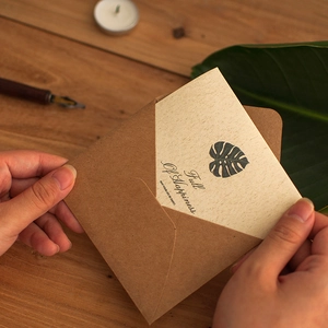 Vintage kraft greeting card with monstera leaf and envelope on a wooden desk